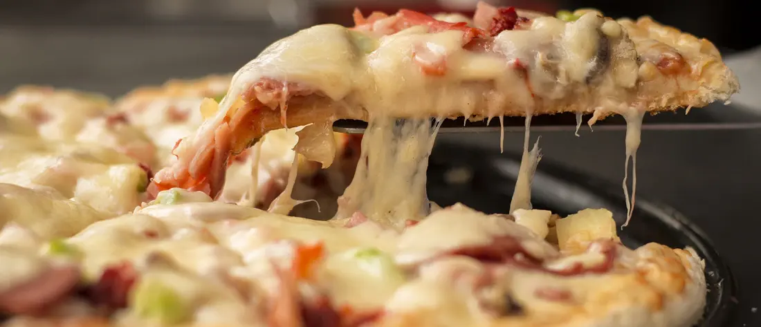 A slice of cheese pizza lifted from the pan, cheese stretching