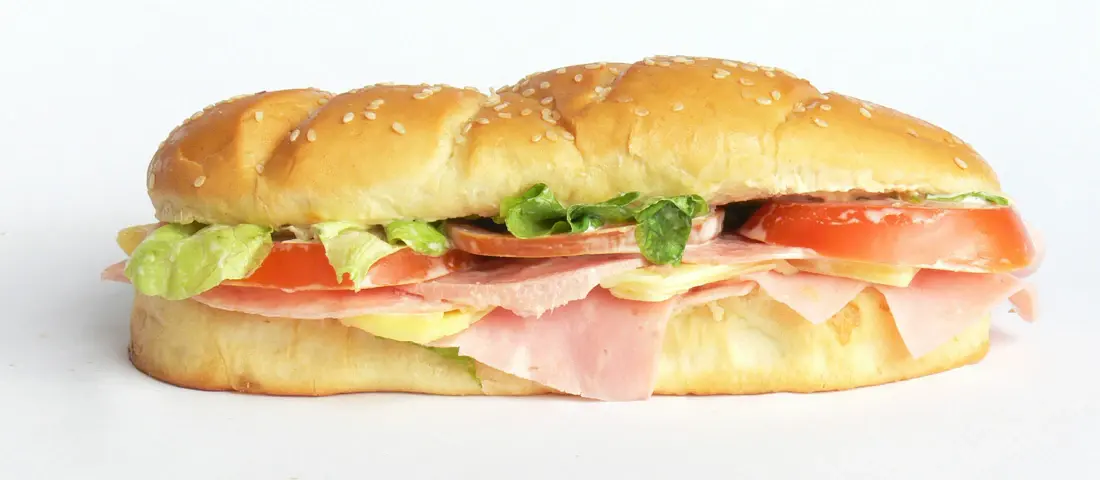 A ham and turkey grinder with lettuce and tomato on a seeded roll